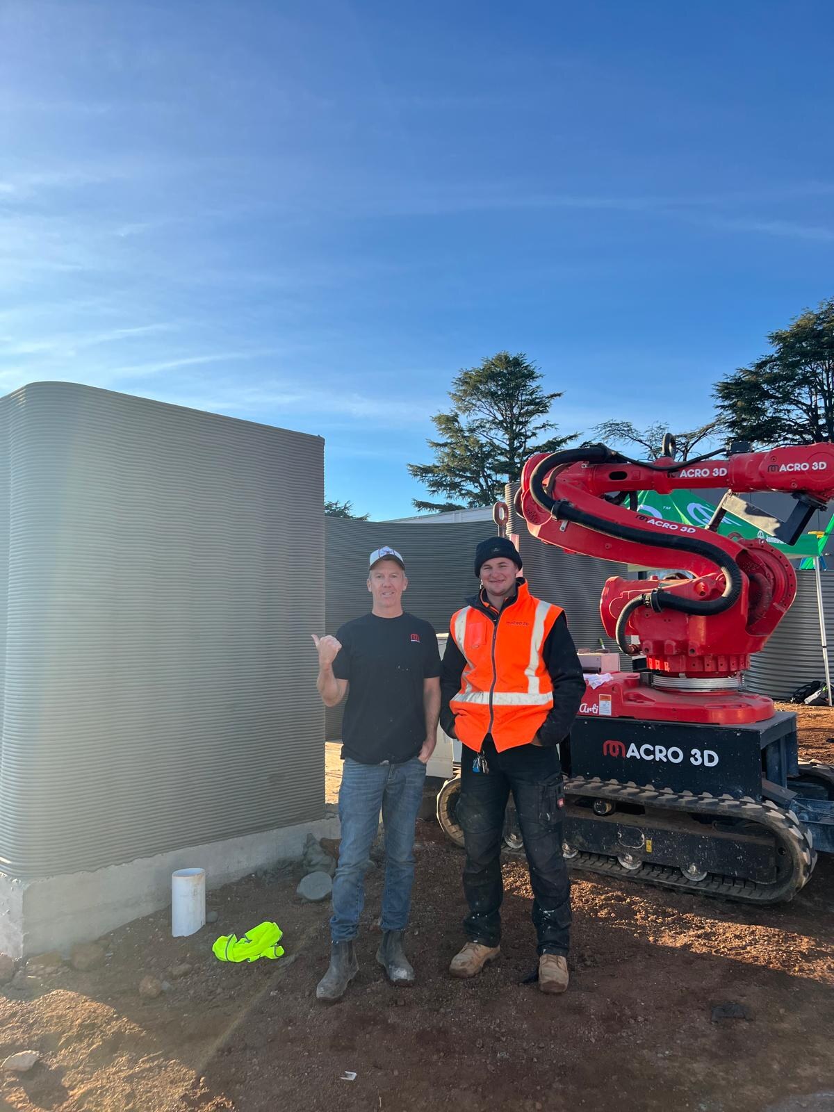 Macro3D team standing beside the red printing robot on site